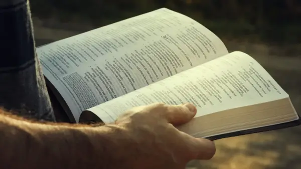 A hand holds open a Bible, revealing the words of Agur in the Bible, Proverbs 31:2.