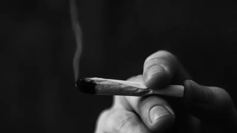 A hand holds a lit joint, smoke curling upwards. This image prompts reflection on whether Christians can smoke weed.